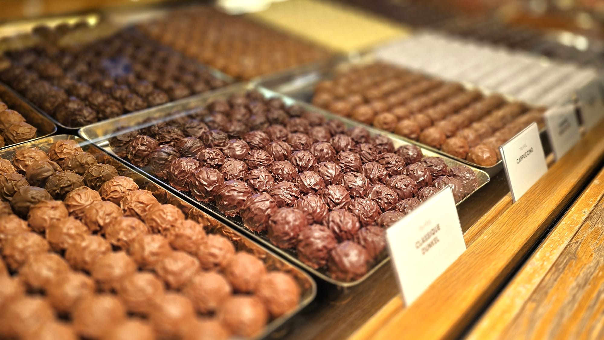 Nahaufnahme der Sprüngli-Verkaufstheke mit handgefertigten Pralinen in verschiedenen Sorten, kunstvoll arrangiert und beschriftet.